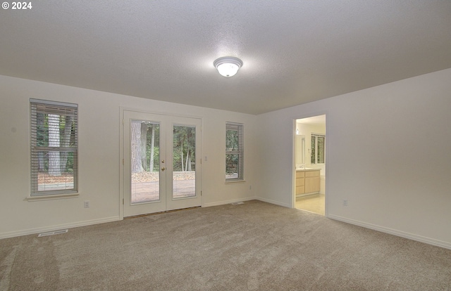 spare room featuring visible vents, a textured ceiling, french doors, baseboards, and light colored carpet