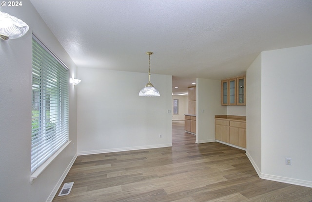 spare room featuring light wood-type flooring, visible vents, baseboards, and a textured ceiling