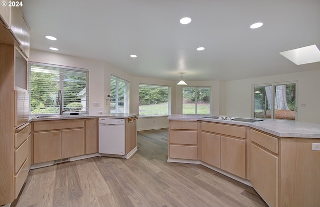 kitchen featuring dishwasher, a skylight, light brown cabinets, and a sink