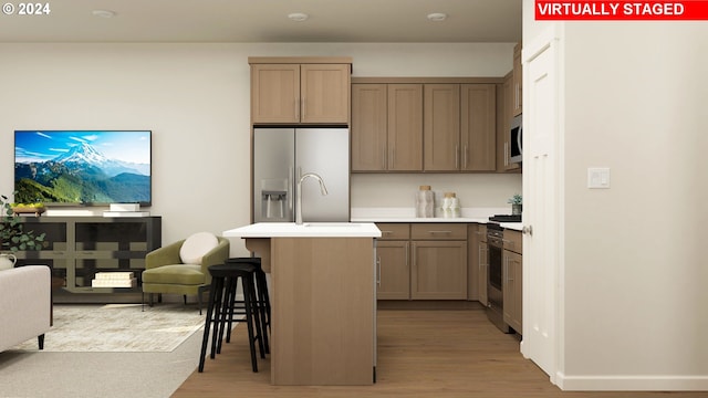 kitchen featuring sink, light wood-type flooring, a center island with sink, a breakfast bar, and appliances with stainless steel finishes