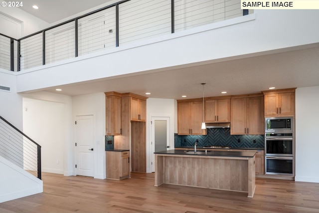 kitchen with built in microwave, a center island with sink, light hardwood / wood-style flooring, a high ceiling, and hanging light fixtures