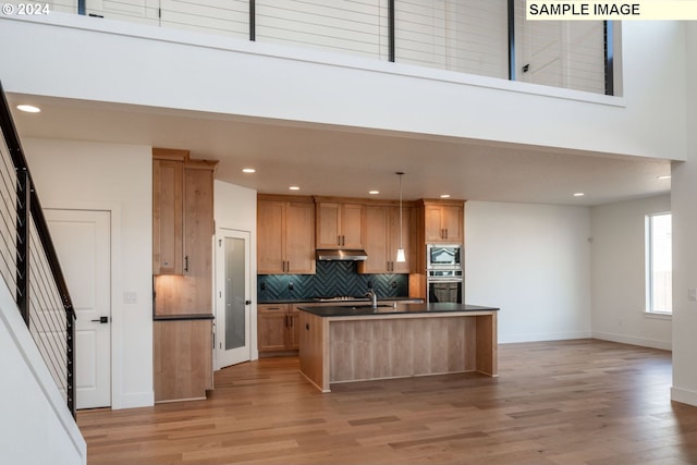 kitchen with appliances with stainless steel finishes, light wood-type flooring, backsplash, pendant lighting, and an island with sink