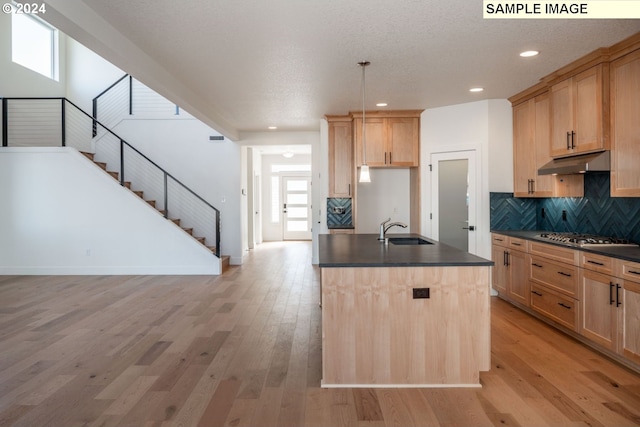 kitchen featuring sink, stainless steel gas cooktop, light brown cabinetry, a center island with sink, and light wood-type flooring