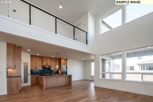 kitchen featuring pendant lighting, decorative backsplash, a towering ceiling, and light hardwood / wood-style flooring