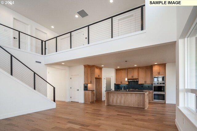 kitchen featuring appliances with stainless steel finishes, tasteful backsplash, pendant lighting, a high ceiling, and an island with sink