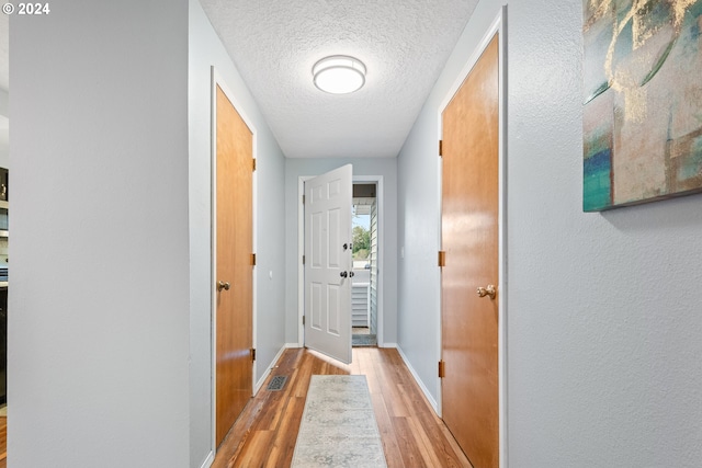 hall with light wood-type flooring and a textured ceiling