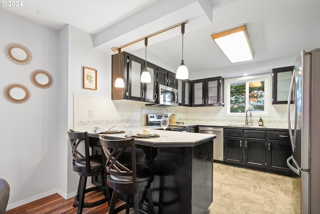 kitchen featuring stainless steel appliances, tasteful backsplash, sink, kitchen peninsula, and decorative light fixtures