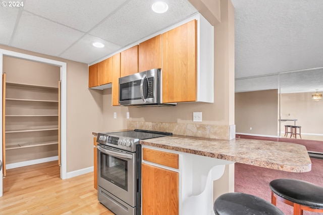 kitchen featuring a drop ceiling, stainless steel appliances, kitchen peninsula, light hardwood / wood-style floors, and a breakfast bar