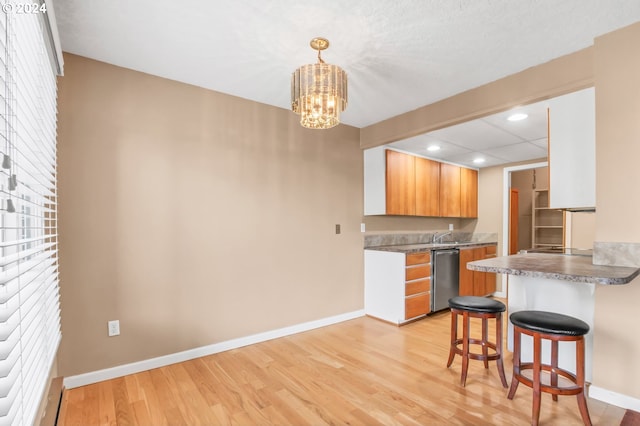 kitchen with pendant lighting, an inviting chandelier, stainless steel dishwasher, light wood-type flooring, and a breakfast bar area