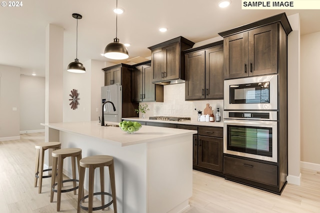 kitchen with dark brown cabinets, decorative light fixtures, and a kitchen island with sink