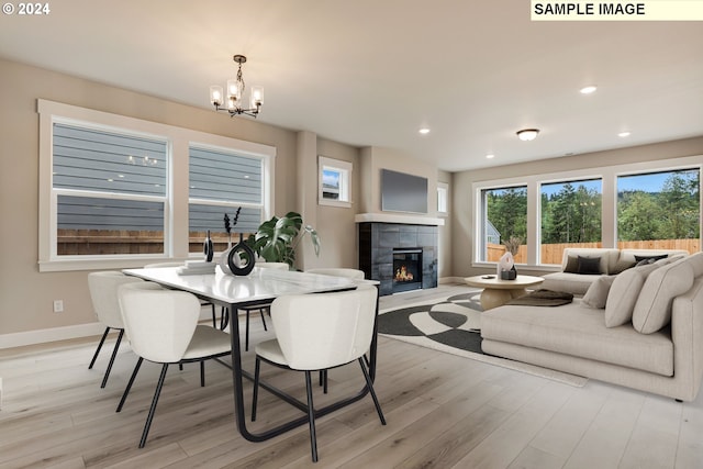 dining space featuring a tiled fireplace, an inviting chandelier, and light wood-type flooring