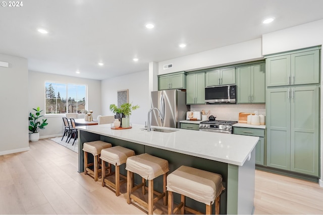 kitchen featuring an island with sink, appliances with stainless steel finishes, green cabinets, and a kitchen breakfast bar