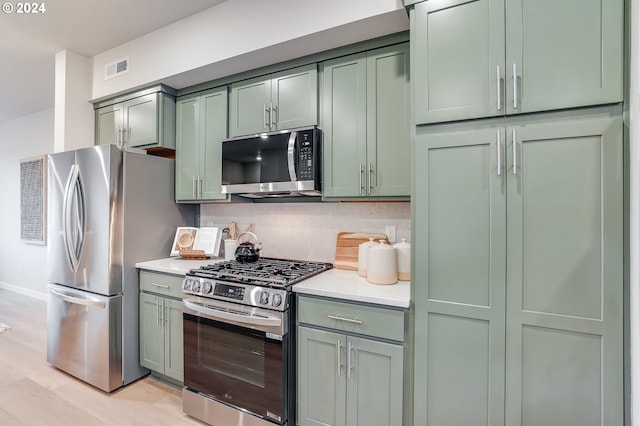 kitchen featuring stainless steel appliances, green cabinets, light hardwood / wood-style floors, and decorative backsplash