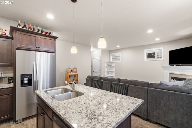 kitchen with sink, an island with sink, appliances with stainless steel finishes, dark brown cabinets, and light stone counters