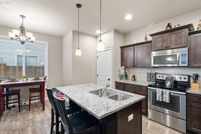 kitchen featuring a kitchen island with sink, hanging light fixtures, sink, dark brown cabinets, and stainless steel appliances