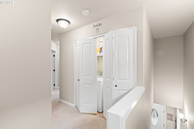 corridor featuring a textured ceiling, light colored carpet, and washer / dryer