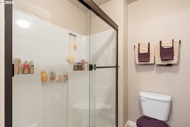 bathroom featuring a shower with door and toilet