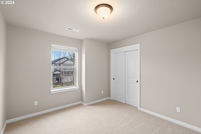 unfurnished bedroom with a textured ceiling, light carpet, and a closet