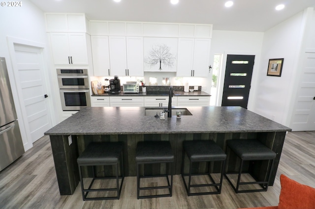 kitchen featuring stainless steel appliances, a kitchen island with sink, sink, and white cabinetry