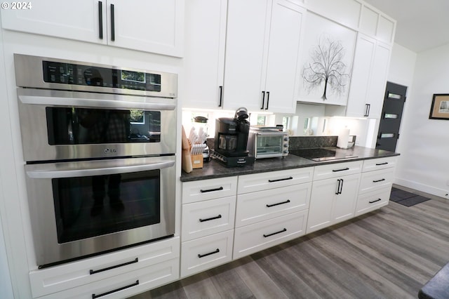 kitchen with black electric stovetop, dark hardwood / wood-style floors, white cabinetry, stainless steel double oven, and dark stone countertops