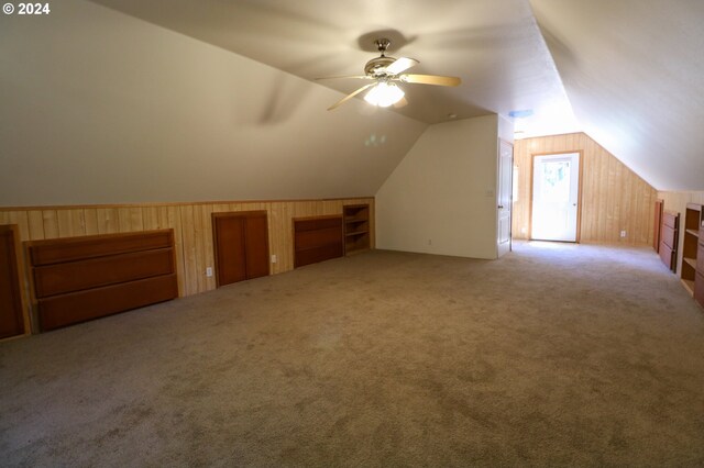 additional living space featuring wood walls, vaulted ceiling, ceiling fan, and light colored carpet