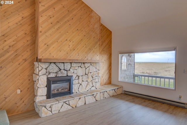 unfurnished living room with wood-type flooring, wooden walls, a stone fireplace, and a baseboard heating unit