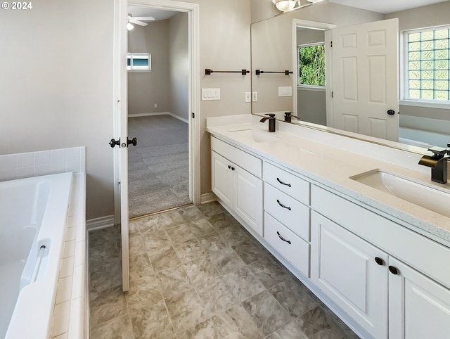 bathroom with ceiling fan, vanity, and tiled bath