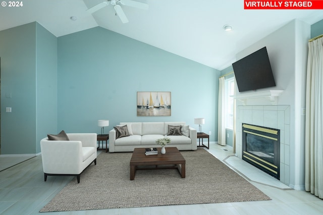 living room with ceiling fan, vaulted ceiling, and a tile fireplace