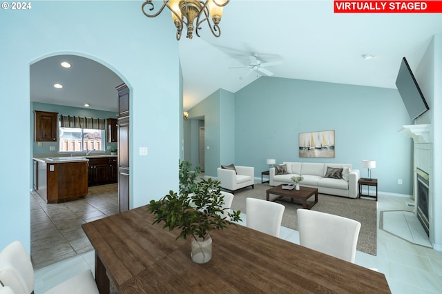 tiled dining area with ceiling fan with notable chandelier, high vaulted ceiling, and a tiled fireplace