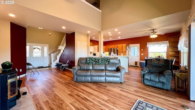 living area with a wood stove, light wood finished floors, stairs, and a high ceiling