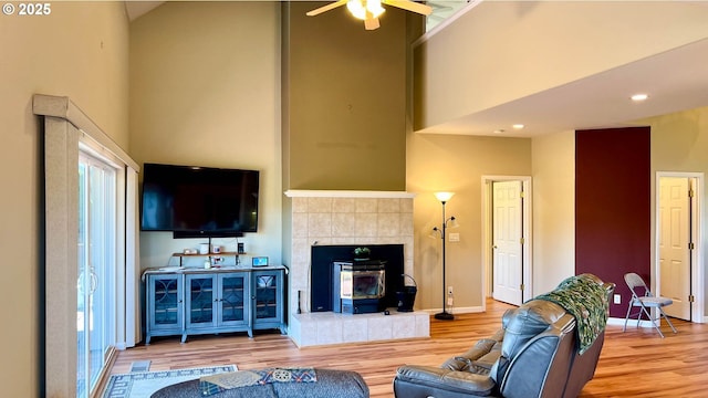 living area featuring a high ceiling, a ceiling fan, a wood stove, wood finished floors, and baseboards