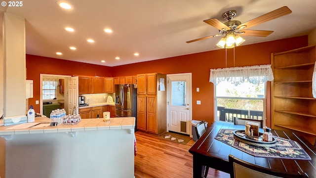 kitchen featuring a peninsula, a healthy amount of sunlight, tile counters, and stainless steel refrigerator with ice dispenser