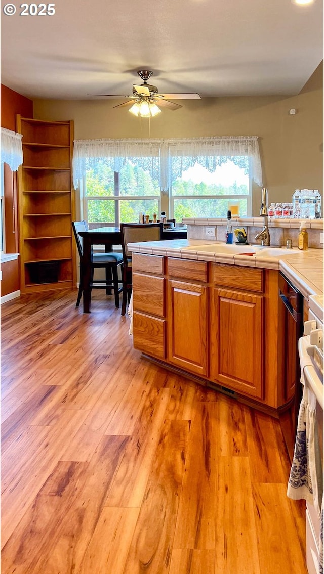 kitchen featuring brown cabinets, tile countertops, a ceiling fan, a sink, and light wood-type flooring