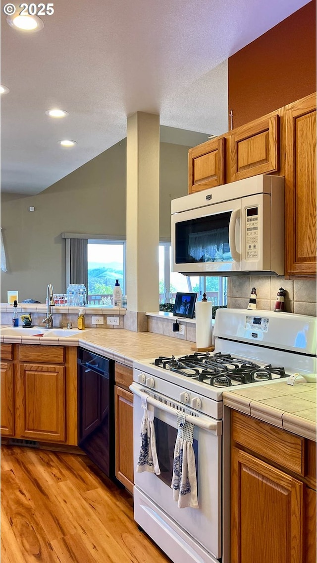 kitchen featuring plenty of natural light, white appliances, brown cabinets, and vaulted ceiling