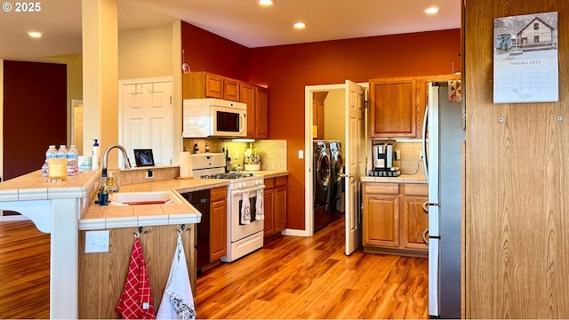 kitchen with tile counters, white appliances, a sink, and a peninsula