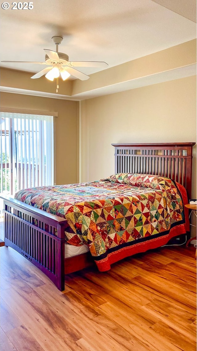 bedroom featuring ceiling fan, a tray ceiling, and wood finished floors