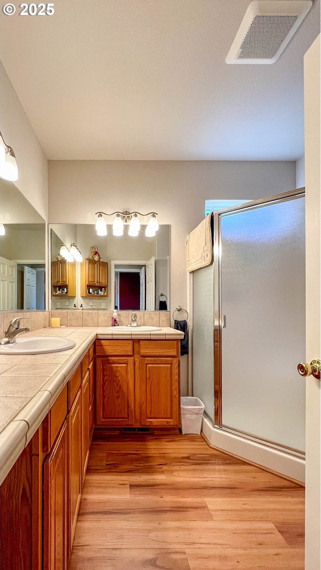 bathroom featuring double vanity, visible vents, a stall shower, a sink, and wood finished floors