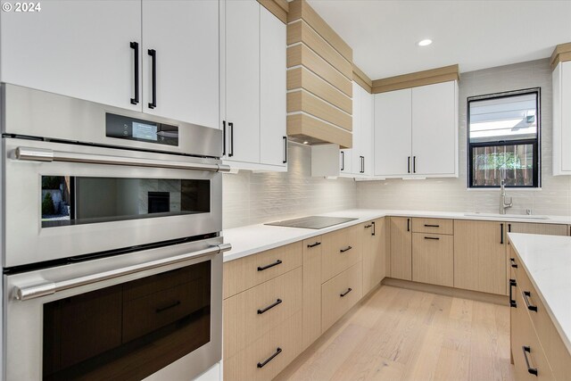 kitchen featuring sink, backsplash, stainless steel double oven, light hardwood / wood-style floors, and white cabinets