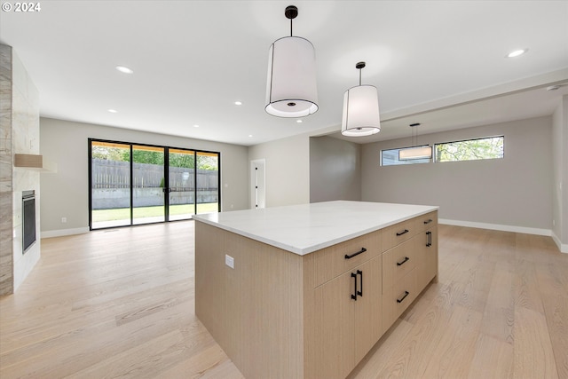 kitchen featuring pendant lighting, a tile fireplace, light stone countertops, light hardwood / wood-style floors, and a kitchen island