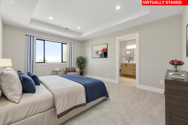 carpeted bedroom featuring a raised ceiling and connected bathroom