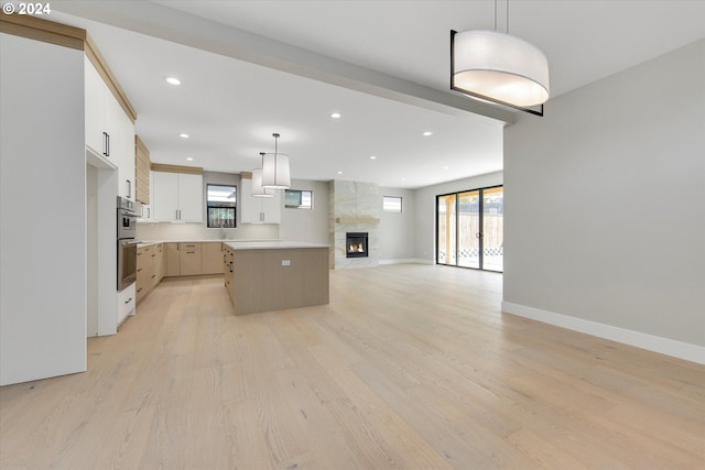 kitchen featuring white cabinetry, a fireplace, a kitchen island, decorative light fixtures, and light wood-type flooring