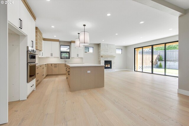 kitchen featuring a tile fireplace, white cabinetry, hanging light fixtures, a center island, and light wood-type flooring