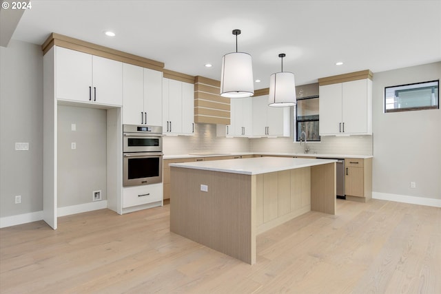 kitchen with white cabinetry, a center island, hanging light fixtures, appliances with stainless steel finishes, and wall chimney range hood