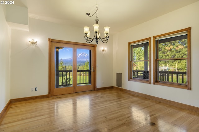 spare room with an inviting chandelier, light wood-type flooring, and a wealth of natural light