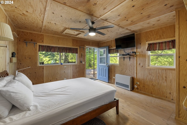 bedroom with multiple windows, wood walls, light hardwood / wood-style flooring, and heating unit