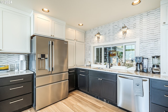 kitchen with backsplash, appliances with stainless steel finishes, light hardwood / wood-style floors, and white cabinets