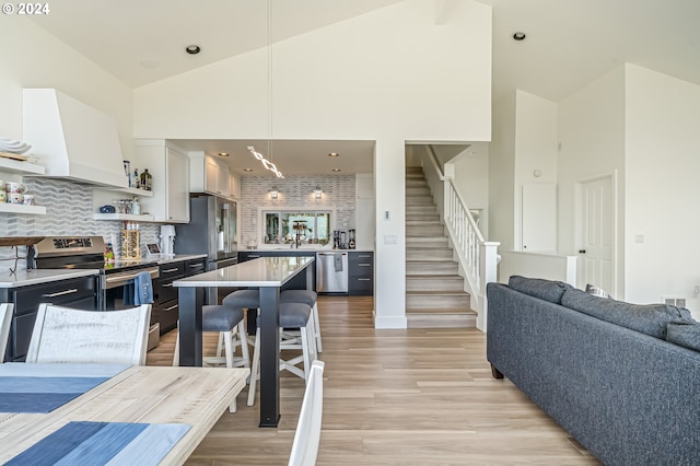 kitchen featuring white cabinetry, appliances with stainless steel finishes, high vaulted ceiling, and a kitchen bar