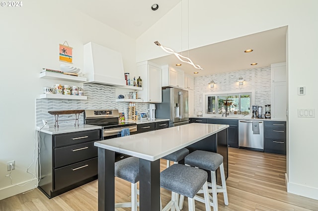 kitchen featuring appliances with stainless steel finishes, decorative light fixtures, white cabinetry, custom range hood, and light hardwood / wood-style flooring