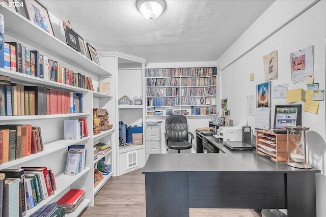 home office with light hardwood / wood-style floors and a textured ceiling