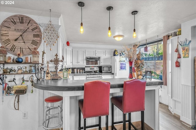 kitchen with decorative light fixtures, a kitchen breakfast bar, appliances with stainless steel finishes, white cabinets, and crown molding